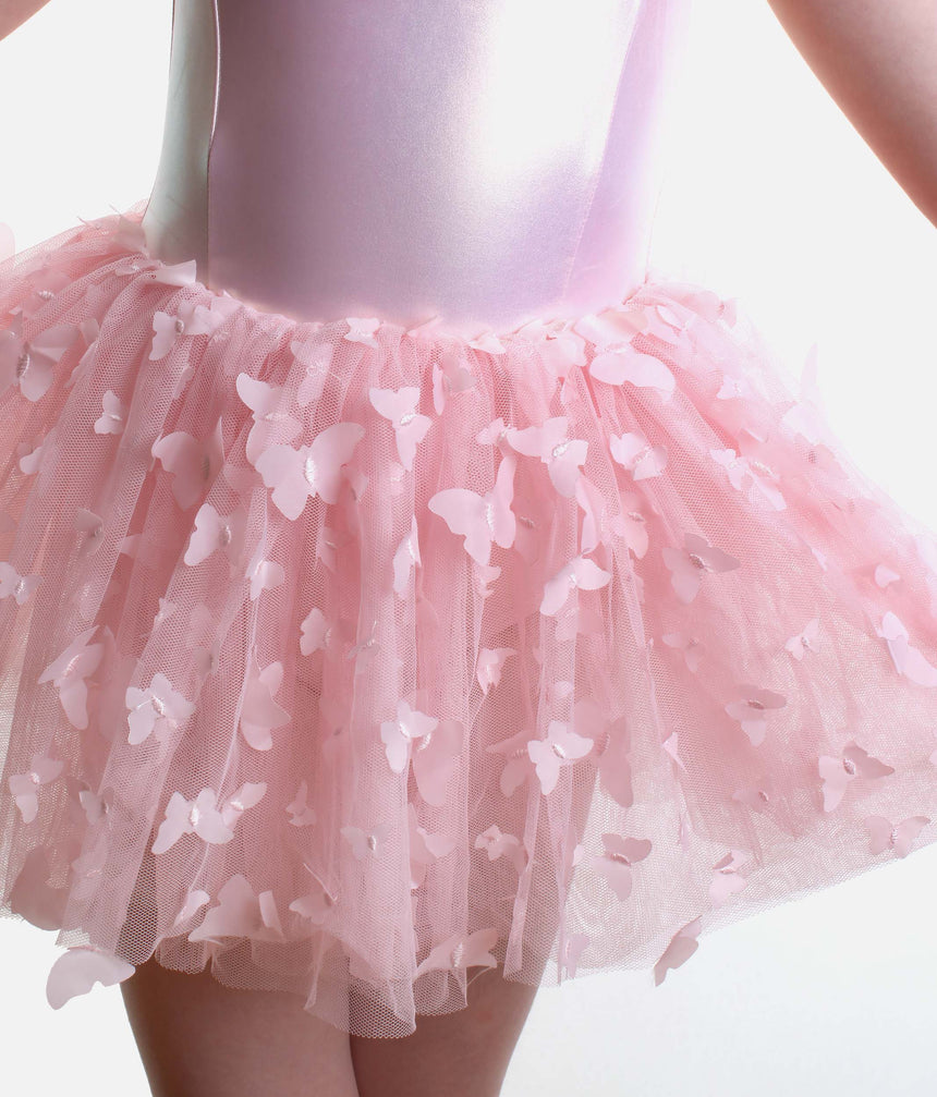 A close-up of a child wearing a light pink tutu skirt with layered tulle and scattered 3D butterfly appliqués, paired with a shiny pale pink bodysuit against a white background.