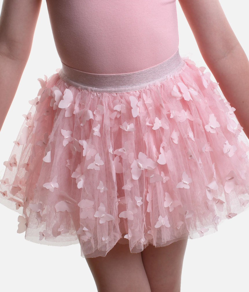 A close-up of a child wearing a pink tutu skirt with 3D butterfly appliqués and a light pink bodysuit against a plain light background.