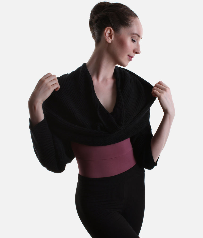 Black Mirella Adagio warm-up scarf worn as a cropped bolero, showing long sleeves and a twisted drape over a plum leotard.