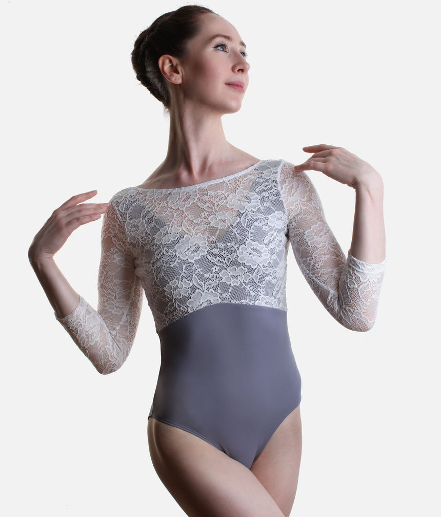 A female dancer wearing a grey and white three-quarter sleeve leotard with a sheer floral lace bodice and solid grey skirt, posed against a light grey studio background.