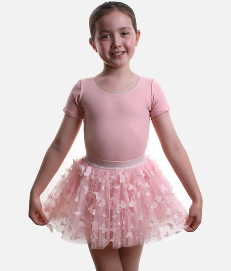 A young girl modeling a pink short-sleeve leotard and a matching pink tulle tutu skirt decorated with small white butterfly appliqués, set against a plain light gray background.