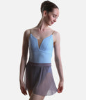 A female dancer wearing a light blue leotard with a deep V-neckline and a sheer gray tulle skirt, posed against a solid light gray background.