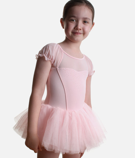 A young girl modeling a light pink ballet leotard with short flutter sleeves, a sheer mesh bodice, and a layered tulle tutu skirt, set against a plain light gray background.