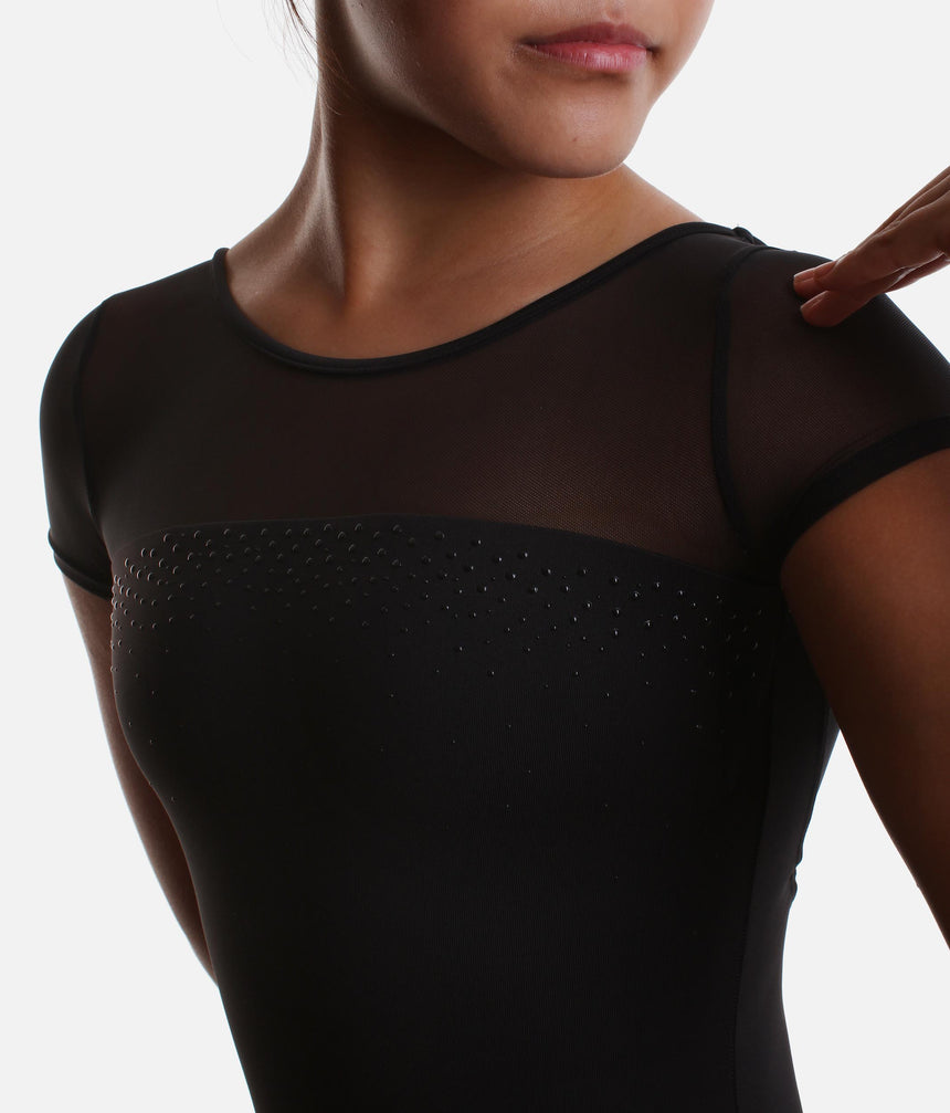 Close-up of a person wearing a black short-sleeve leotard with sheer mesh shoulders and a textured dotted panel across the chest, against a light gray background.