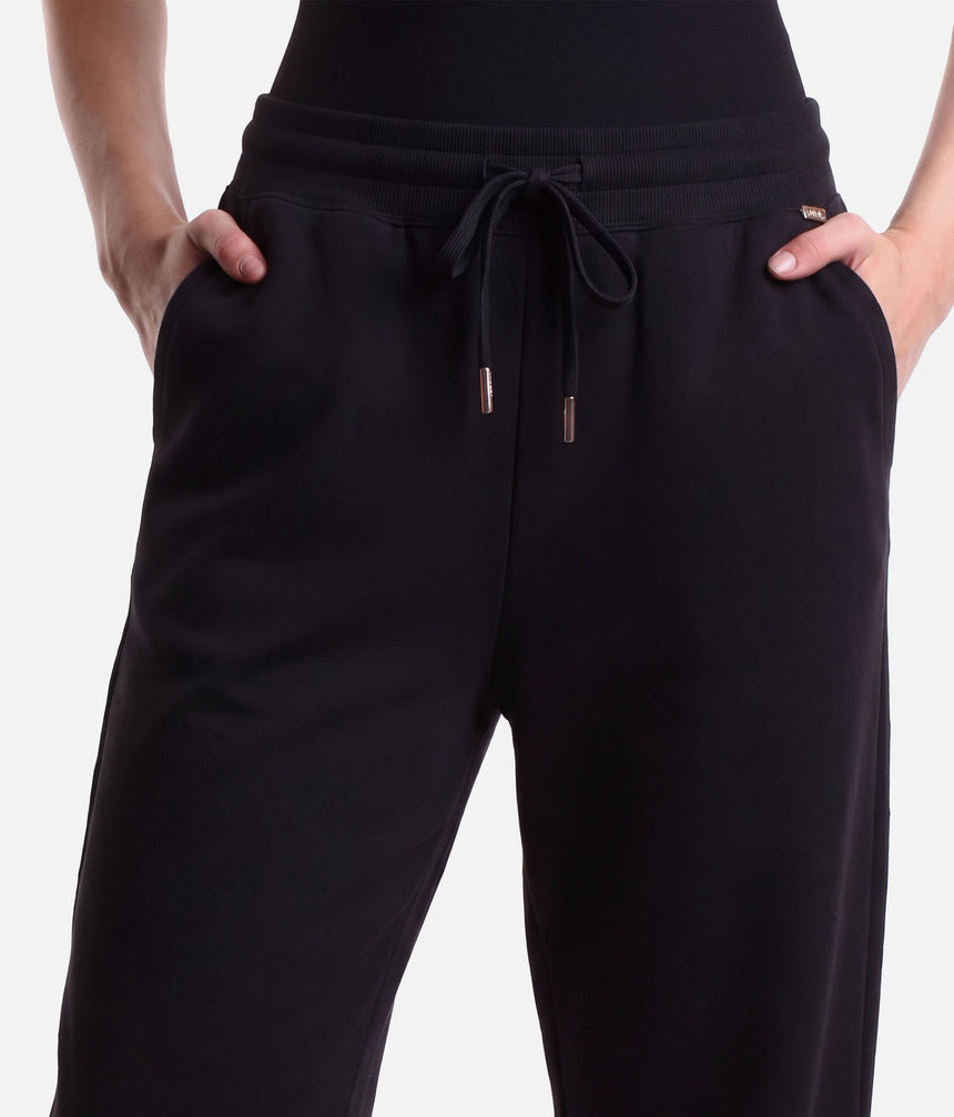 Front view of Mirella Adagio wide leg sweatpants in Black, styled with a black leotard and finished with open hems.