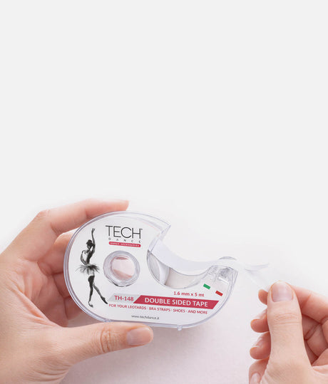 A person's hands holding a roll of TECH brand double-sided tape, with the clear tape being pulled out, against a solid white background.