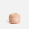 Side view of a peach pink Tendu darning thread ball showing the wound strands on a white background.