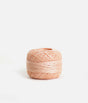 Side view of a peach pink Tendu darning thread ball showing the wound strands on a white background.